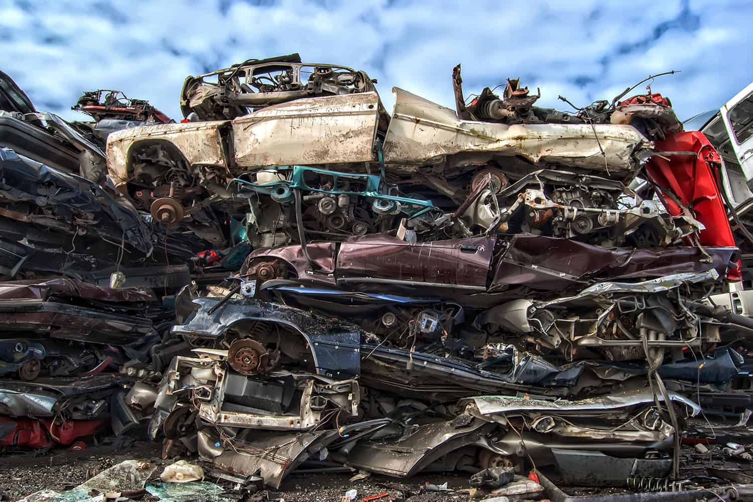 A stack of crushed cars piled under a cloudy sky, showing various colors and metal parts intertwined.