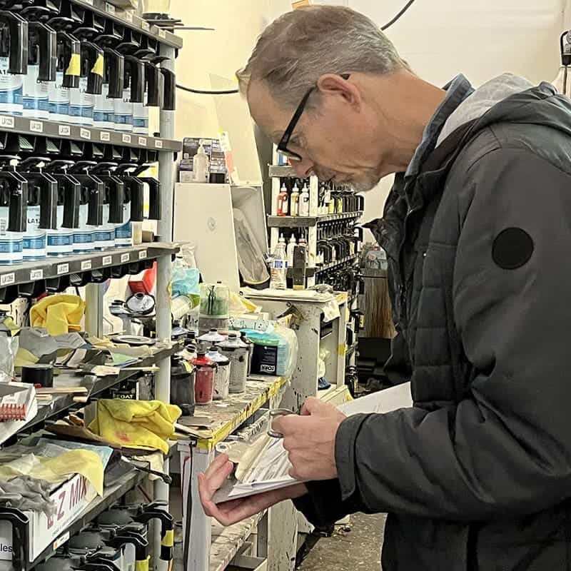 A man makes notes on a clipboard while inspecting paints