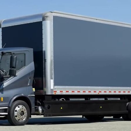 A dark gray box truck parked outdoors on a clear day, with a large rectangular cargo area and visible wheels.